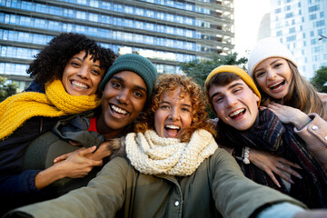 Multiracial group of college friends laughing and having fun together taking selfie during winter looking at camera.