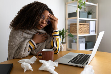 Sick African American woman working from home office having headache while working with laptop.