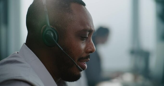 Close up portrait of African American technical support specialist in headset having conversation with client, helping online on phone call. Customer experience officer works in call center office.
