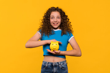 Girl smiling while holding a piggy bank, emphasizing the importance of saving and financial...