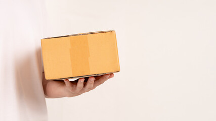 Hand holding cardboard box on empty background. Concept for transportation, online shopping, celebration and gift giving on special day.