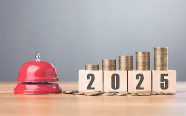 Red bell sits beside a stack of coins placed on a wooden block labeled '2025,' symbolizing financial goals and the urgency of planning for the year ahead