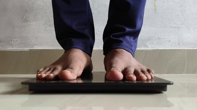Young adult person feet standing on digital weighing scale machine to measure, check body weight or fat. Dieting, obesity, overweight, underweight, fitness, weight loss and healthy lifestyle concept.