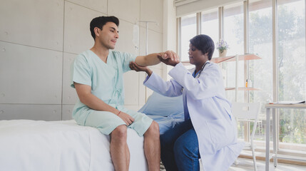 Patient caucasian man with woman nurse carer physical therapist black people two person sitting talk helping support give advice and holding hand arm inside clinic hospital indoor room service.