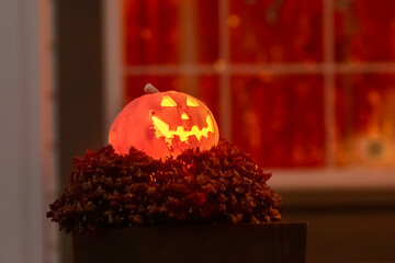 A glowing Halloween pumpkin lantern sits on a bed of dried leaves, its warm light contrasting with the dark background.