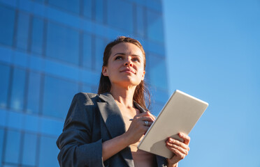 Brunette woman in smart casual attire working on a digital tablet outside a business building.