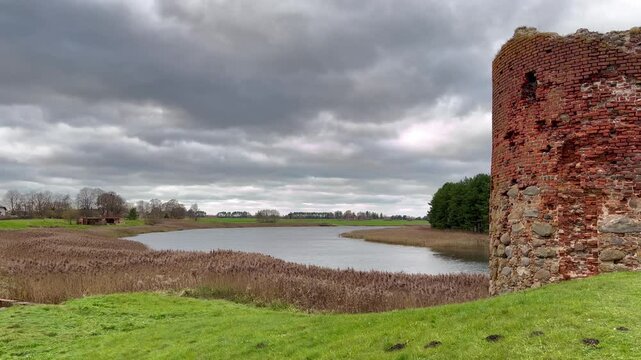 Historic Schmachturm (Shame Tower) of Piltene Castle Overlooking a Serene River Bend Under Dramatic Clouds in Courland, Latvia - Static Video