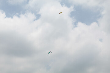 Two parachutes of paragliders with cloudy sky background
