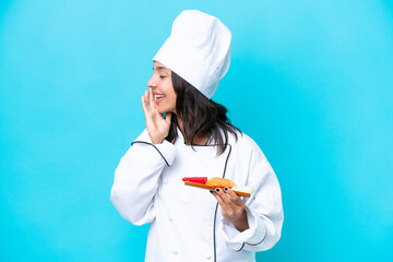 Young hispanic chef woman holding sashimi isolated on blue background shouting with mouth wide open to the side
