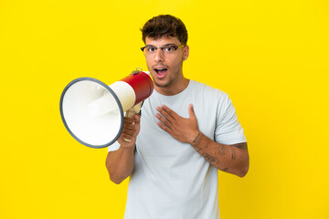Young caucasian handsome man isolated on yellow background shouting through a megaphone with surprised expression