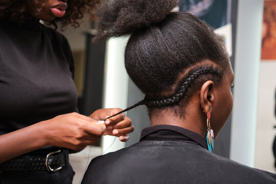 Hairdresser braiding client's afro hair in salon