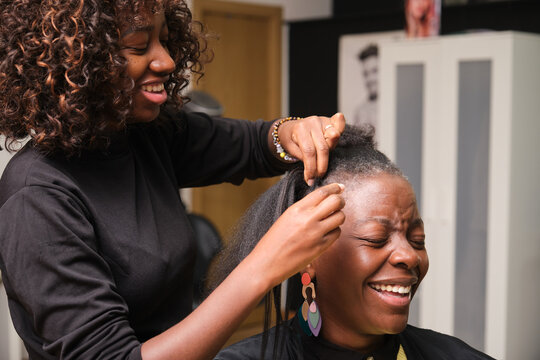 Hairdresser braiding client's afro hair in salon