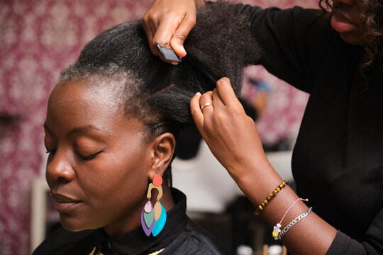 Hairdresser braiding client's afro hair in salon