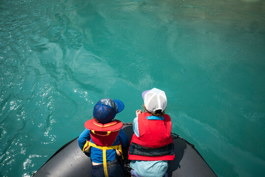 Two young children lean over a raft looking into turquoise water.