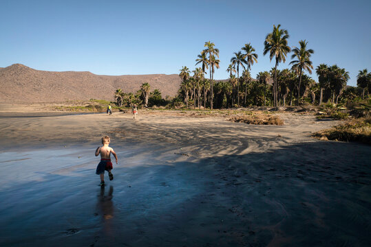 A 3-year-old boy runs down a wide beach with palm trees.