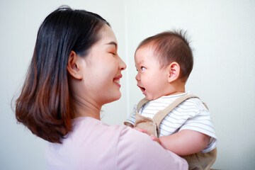The mother is holding a baby and smiling.