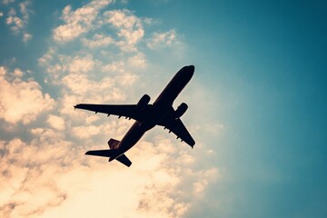 Silhouette of passenger airplane flying in cloudy sky at sunset