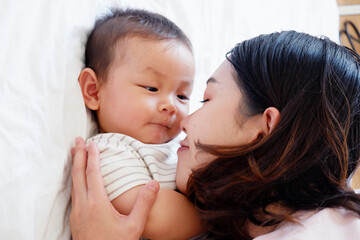 A mother and her cute little baby are lying on a white bed.