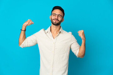 Young caucasian man isolated on blue background doing strong gesture