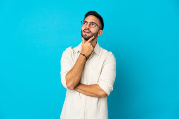 Young caucasian man isolated on blue background having doubts