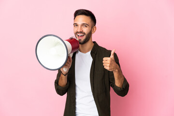 Young caucasian man isolated on pink background shouting through a megaphone to announce something...