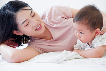 A mother and her cute little baby are lying on a white bed.