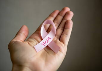 A hand holds a pink ribbon symbolizing hope and awareness for breast cancer during a supportive moment