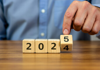 Naklejka premium Man flipping a block from 4 to 5 while showing the year 2025 on a wooden table
