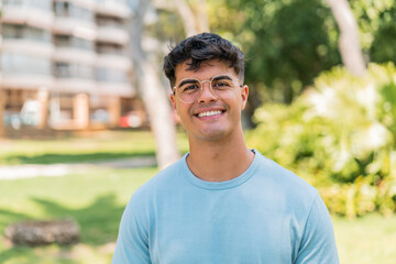 Young hispanic man at outdoors With glasses with happy expression