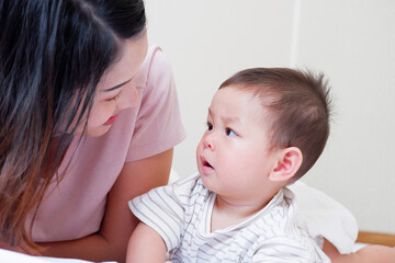 A mother and her cute little baby are lying on a white bed.