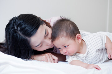 A mother and her cute little baby are lying on a white bed.