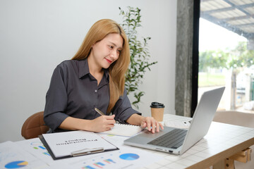 A woman is sitting at a desk with a laptop and a notebook