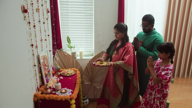 Long shot of family gathering to perform traditional Diwali puja, offering prayers in front of decorated altar with lights, flowers, and sweets, symbolizing devotion, unity, and blessings