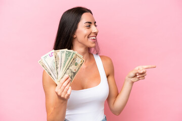 Young caucasian woman taking a lot of money isolated on pink background pointing to the side to present a product