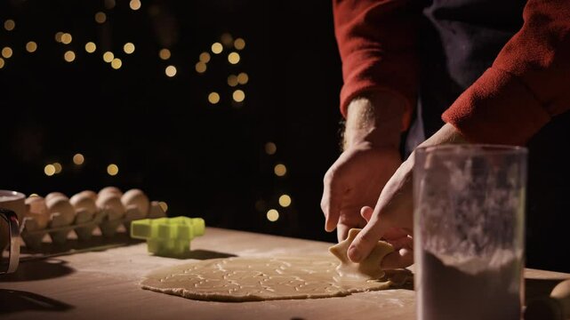 Man Preparing Christmas gingerbread cookies in his kitchen, close-up. Hands cutting out shapes for Christmas cookies from ginger dough with plastic mold on the table.