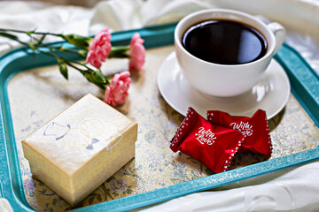 Romantic breakfast. Elegant breakfast tray with cup of black coffee, red wrapped chocolates, gift box, and pink flowers. Perfect for special occasions and romantic mornings. Valentine's Day