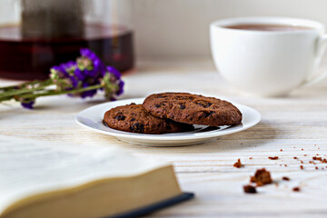 Breakfast. Cozy setting with chocolate cookies on plate, cup of tea and sprig of purple flowers. Perfect for relaxation and comfort themes