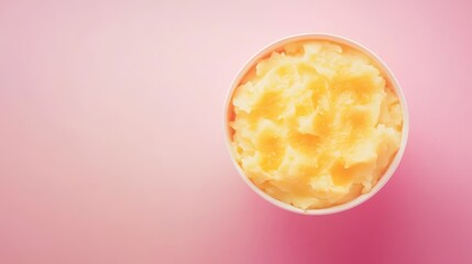 A close-up overhead shot of a small white container filled with yellow-colored whipped shea butter on a pink background.