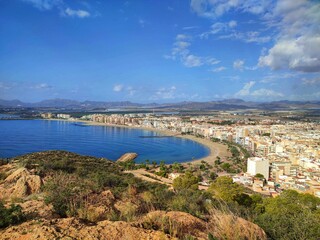A panoramic view of Águilas city, with densely packed buildings and mountainous background under a partly cloudy sky