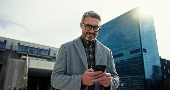 CEO, mobile and businessman typing in city for urban planning, schedule or reading email. Phone, smile and mature manager outdoor to scroll chat app for text, travel or news notification on internet