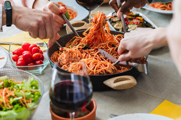 Friends sharing delicious spaghetti with tomato sauce during lunch