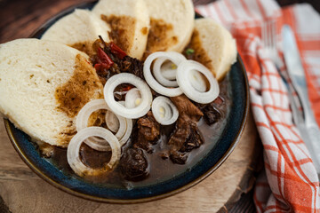 Traditional Czech Beef Goulash with Bread Dumplings and Onions in a Rustic Setting