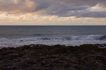 Waves crashing into coastal rocks at sunset. Dramatic sea coast background. Raglan, New Zealand