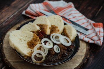 Traditional Czech Beef Goulash with Bread Dumplings and Onions in a Rustic Setting