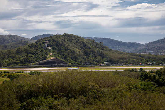 A beautiful small airport in the middle of the jungle. Clouds in the sky. Green trees. A plane on the runway.