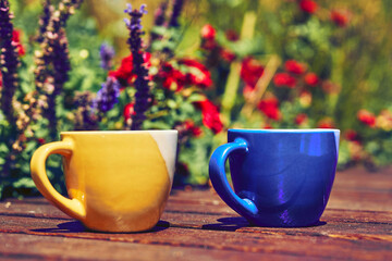 Tea time. Coffee break. Blue yellow cups on wooden in blooming garden