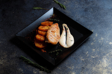 Grilled chicken steak with spices and baked potatoes on a black plate on a dark textured background with copy space.