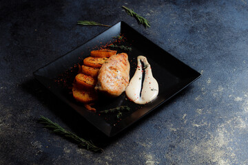 Grilled chicken steak with spices and baked potatoes on a black plate on a dark textured background with copy space.