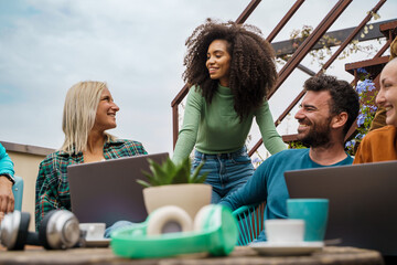 Digital nomads students working together at outdoor cafe garden terrace - diverse remote workers...
