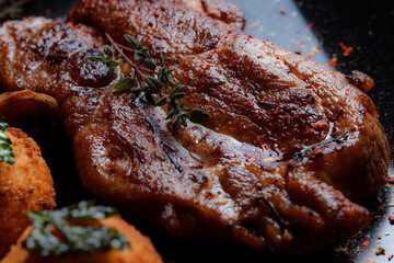 Very close-up turkey steak in caramelized sauce with potato balls on a black plate. Spices - ground pepper, parsley, basil, thyme, white garlic sauce. Detailed texture of fried meat.